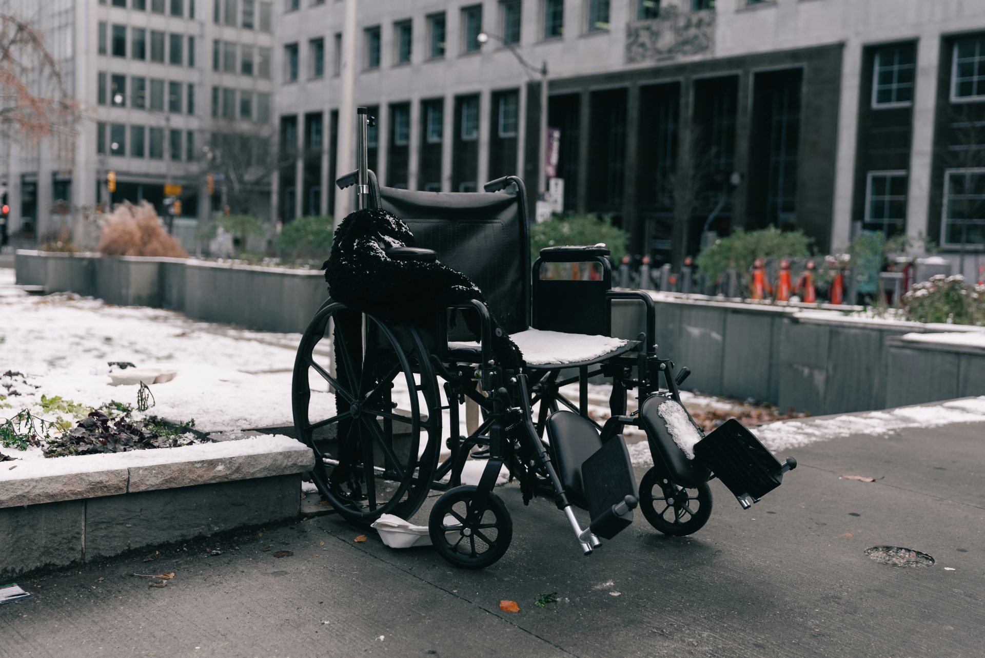 A wheelchair sits abandoned on a snowy sidewalk.